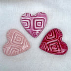 Three ceramic hearts in different pink shades on a white fabric background.