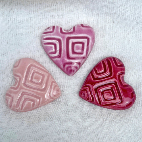 Three ceramic hearts in different pink shades on a white fabric background.