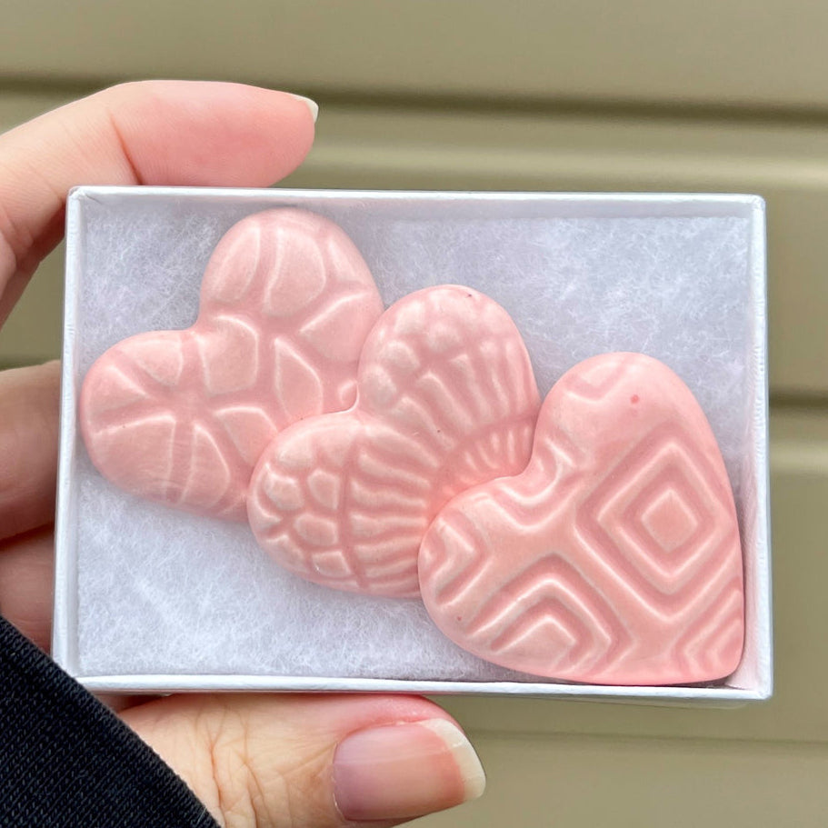 Hand holding a small box with pink heart-shaped objects against a beige background