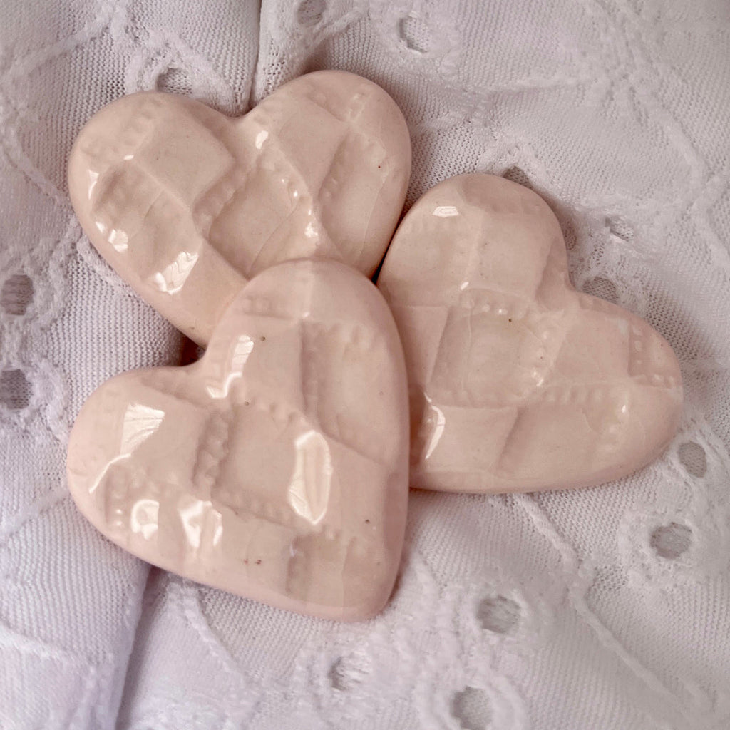 Three light pink heart-shaped ceramics on a textured white background.