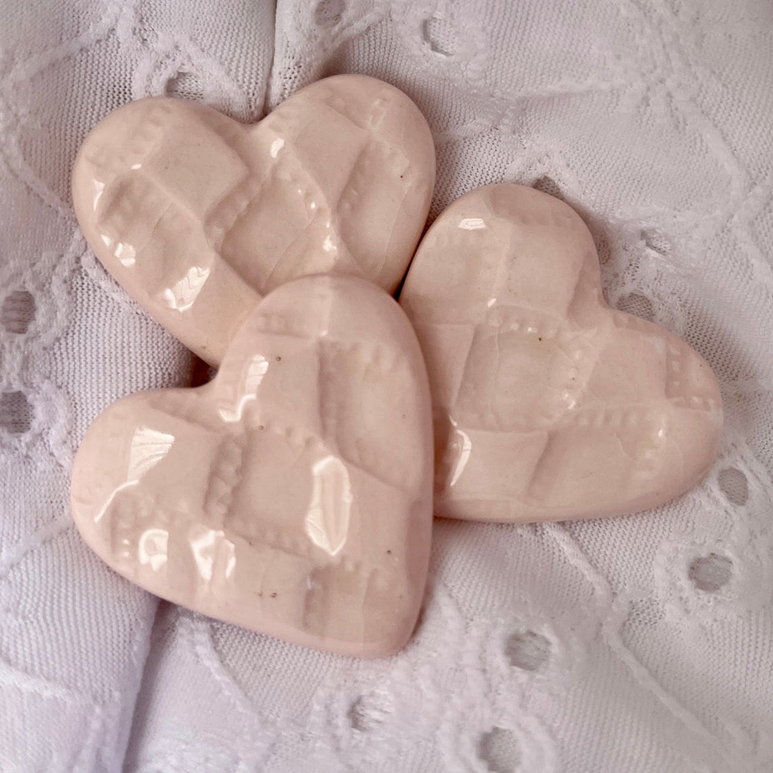 Three light pink heart-shaped ceramics on a textured white background.