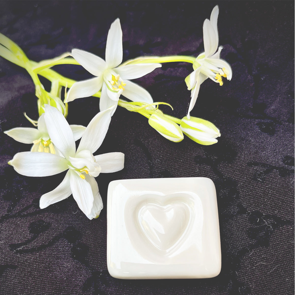 White ceramic with a heart design and white flowers on a dark background, labeled 'LOVE STONES'.