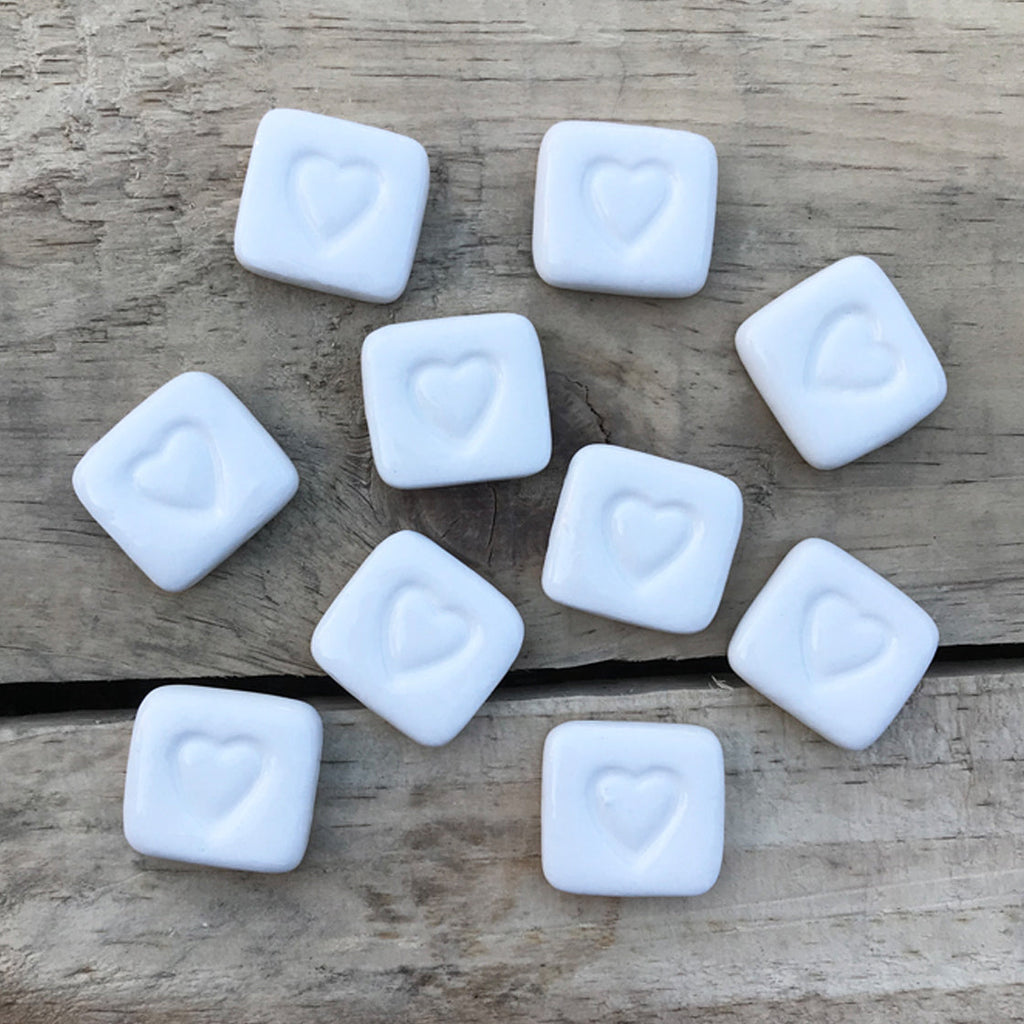 White square stones with heart imprints on a wooden surface, labeled 'Love Stones'.