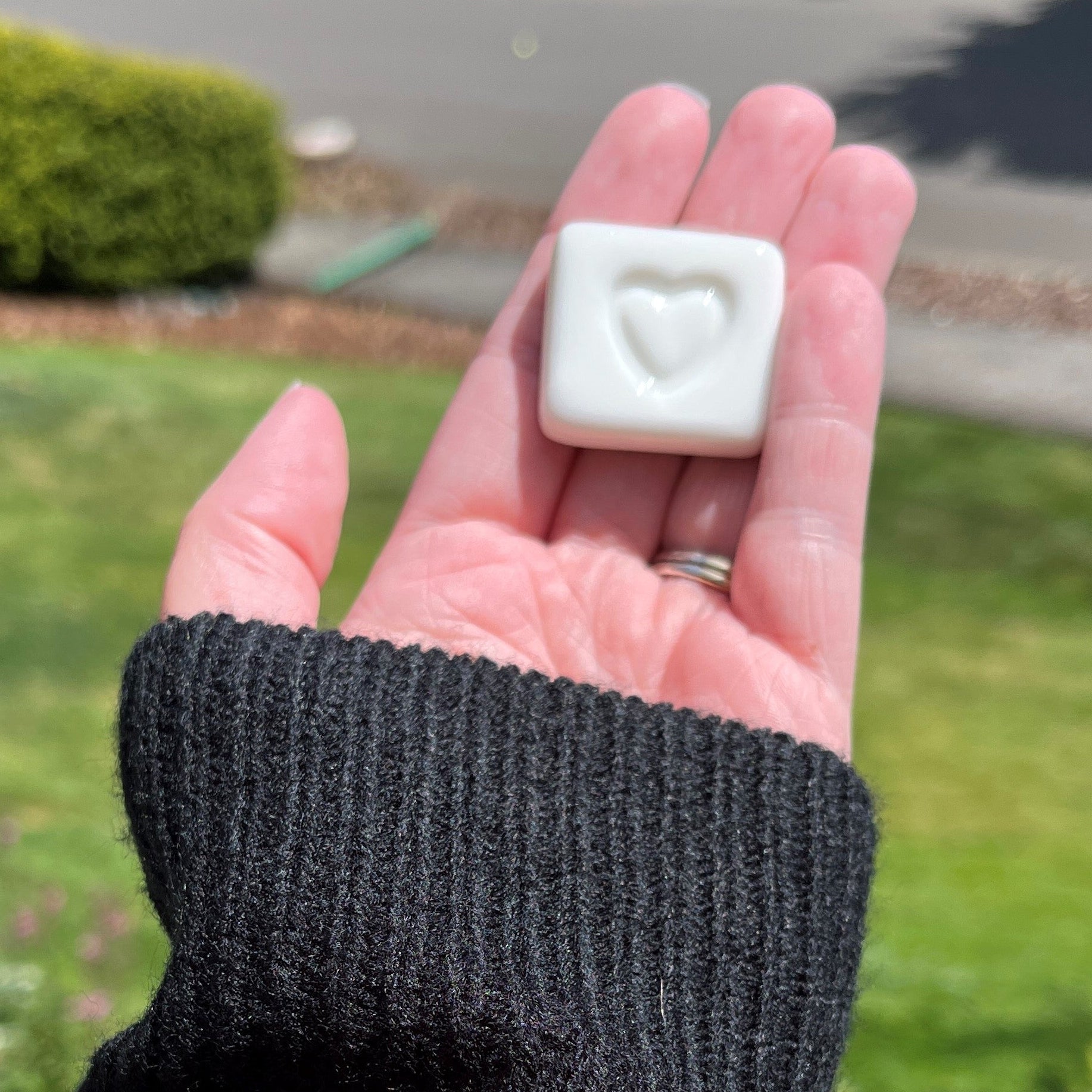 Hand wearing a black knit sweater holding a small white ceramic with a heart print.